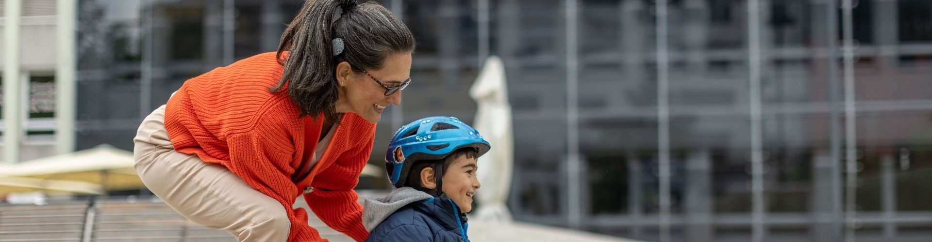 A woman is helping a boy to skateboard, and she is able to hear his laughter thanks to her cochlear implant.